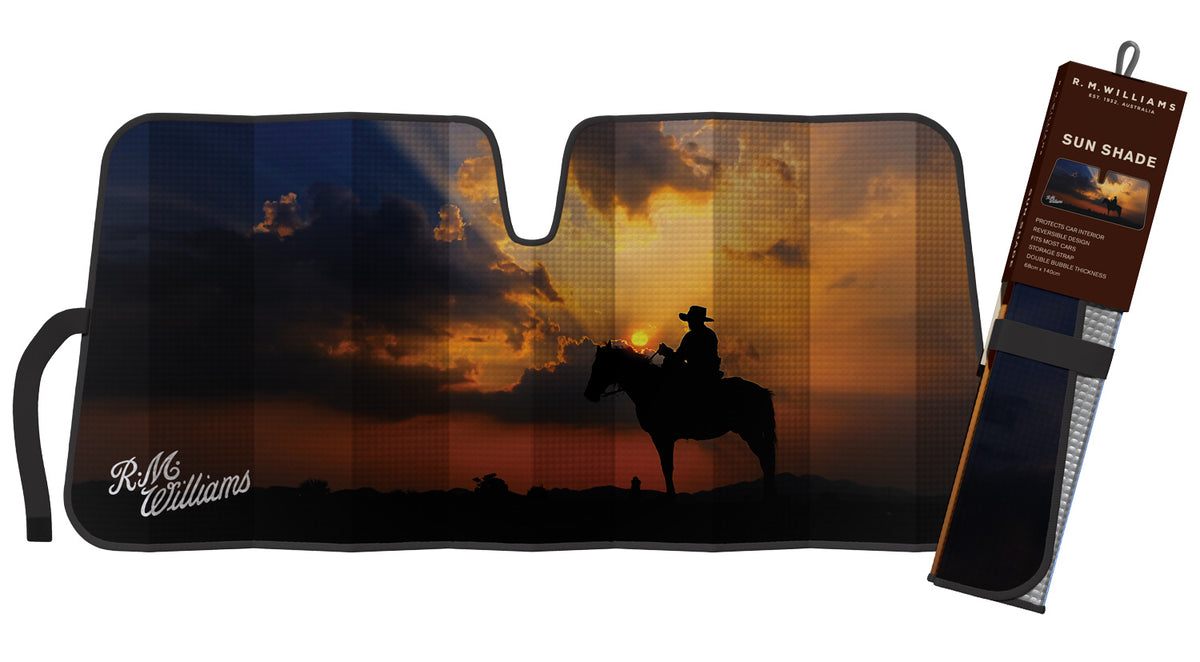 Introducing the RM Williams Sunrise Sunshade, adorned with a striking silhouette of a cowboy on horseback set against a vibrant sunset. "R.M. Williams" is elegantly printed in white at the bottom left corner. Complete with a storage strap for easy handling, it fits seamlessly on your windshield. The right side of the packaging showcases the same captivating design and branding details.