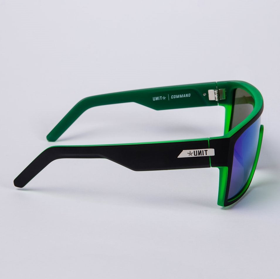 Introducing the UNIT Command Polarised Eyewear: This pair of sporty sunglasses boasts a lightweight green and black frame paired with blue-tinted, UV-protected lenses. The inside of the arm showcases white text that reads "UNIT" and "COMMAND," while the exterior features a sleek "UNIT" logo. Its modern design ensures both style and protection.
