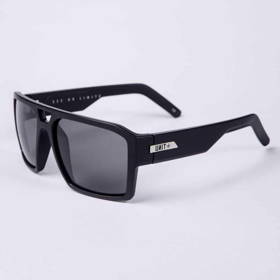 The UNIT Vault Polarised Eyewear is a pair of black sunglasses with thick square frames and dark-tinted polycarbonate polarized lenses. The temples feature a metal plate with the brand name "UNIT" and an arrow symbol. Offering UV protection, the lightweight frame ensures comfort, while the inner side of the temples reads "SEE NO LIMITS.