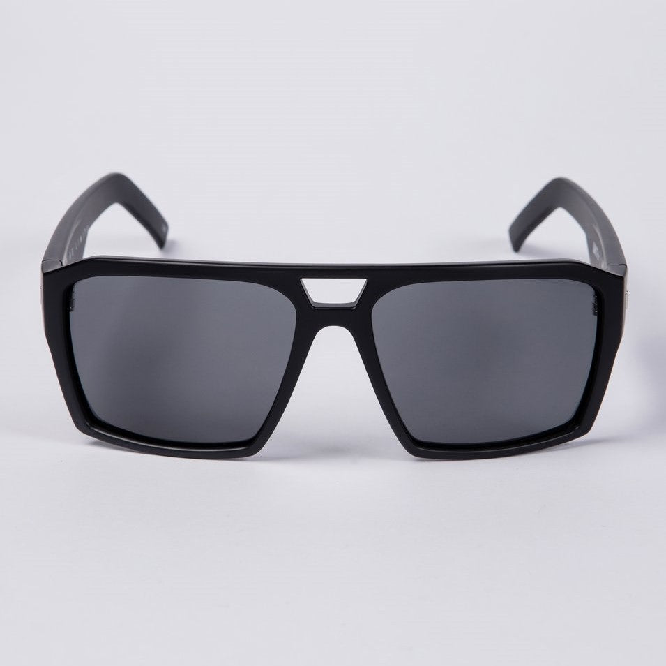 The UNIT Vault Polarised Eyewear is showcased against a plain white background, featuring black sunglasses with a thick, angular frame and dark polycarbonate polarized lenses. The bridge of the sunglasses sports a distinctive triangular gap at the top for added style.