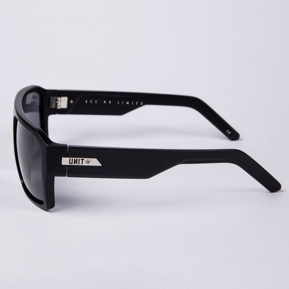 Introducing the UNIT Vault Polarised Eyewear: a sleek pair of black sunglasses with "SEE NO LIMITS" inscribed on the inside arms. These stylish sunglasses feature polycarbonate polarized lenses that offer UV protection and a lightweight frame for comfort. The modern design is highlighted by a silver logo and detailing on the arms, while the dark rectangular lenses strikingly contrast against any background.