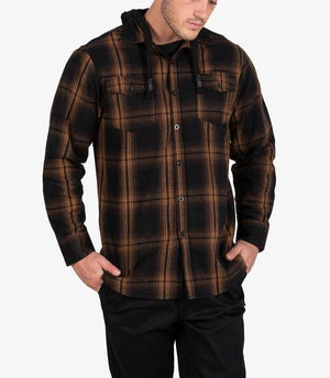 A man wears the UNIT Chester Hood Flannel Shirt, featuring a black and brown plaid design, standing with hands in pockets against a plain light background.