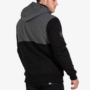 A man faces away wearing the UNIT Terrace Fleece Hoodie, which is fleece lined and two-tone with a dark gray top, black bottom, UNIT logo on the upper arm, and paired with black pants.