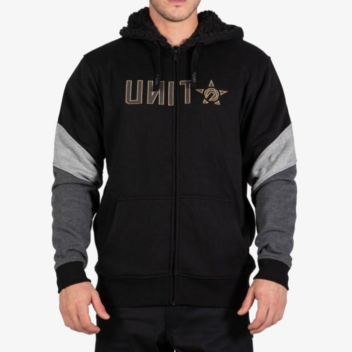 Wearing the UNIT Graded Fleece Hoodie, featuring a black body, gray sleeve panels, a sherpa-lined hood, and bold gold "UNIT" lettering in backward font across the chest.