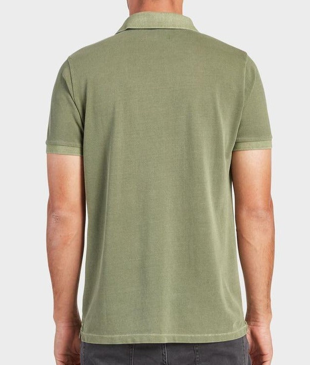 A person wearing an Academy Brand Academy Polo in light green and dark pants is shown from the back. The comfortable cotton pique fabric offers a relaxed feel as the person's arms rest by their sides against a plain light gray background.