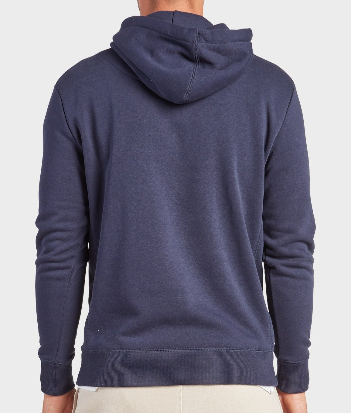 A person is seen from behind wearing the Academy Brand College Hoodie in dark blue. The plain, long-sleeve sweatshirt pairs with light pants, creating a casual look against a plain, light background.