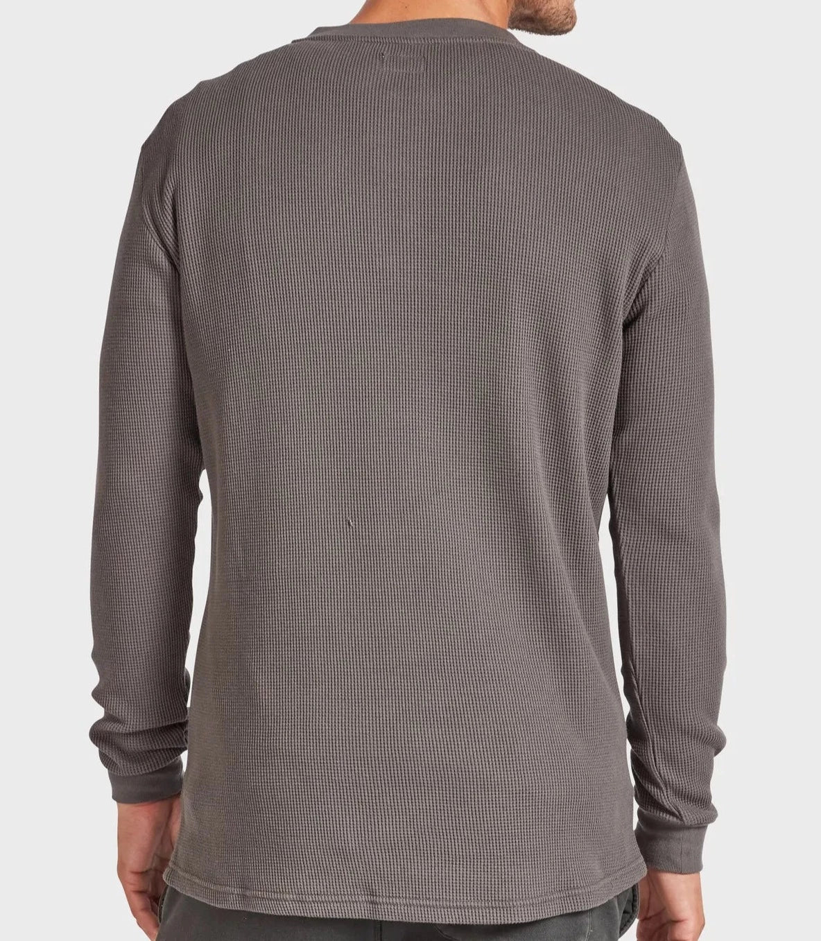 A person in an Academy Brand Sycamore Henley, a grey, long-sleeve, waffle-knit shirt, is shown from the back. They are standing against a plain, light-colored background with their right arm slightly bent and this stylish jumper hanging loosely over their pants.