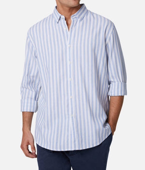 A man is wearing the Industrie The Barco Shirt, a light blue and white vertical striped button-up casual shirt with a collar and white buttons. The relaxed fit shirt is made from 100% cotton, has its sleeves rolled up, and is paired with dark pants. His head is not visible in the image.