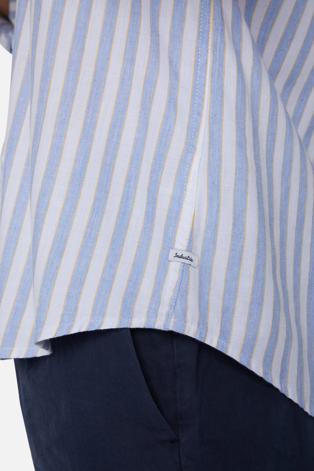 A close-up of a person wearing the Industrie The Barco Shirt, featuring blue and white vertical stripes, crafted from 100% cotton and tucked into dark blue pants.