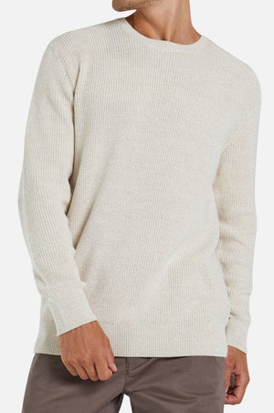 A person wearing the Industrie The Kingston Knit, a cream-colored, long-sleeve waffle knit sweater, and brown pants stands against a plain white background.