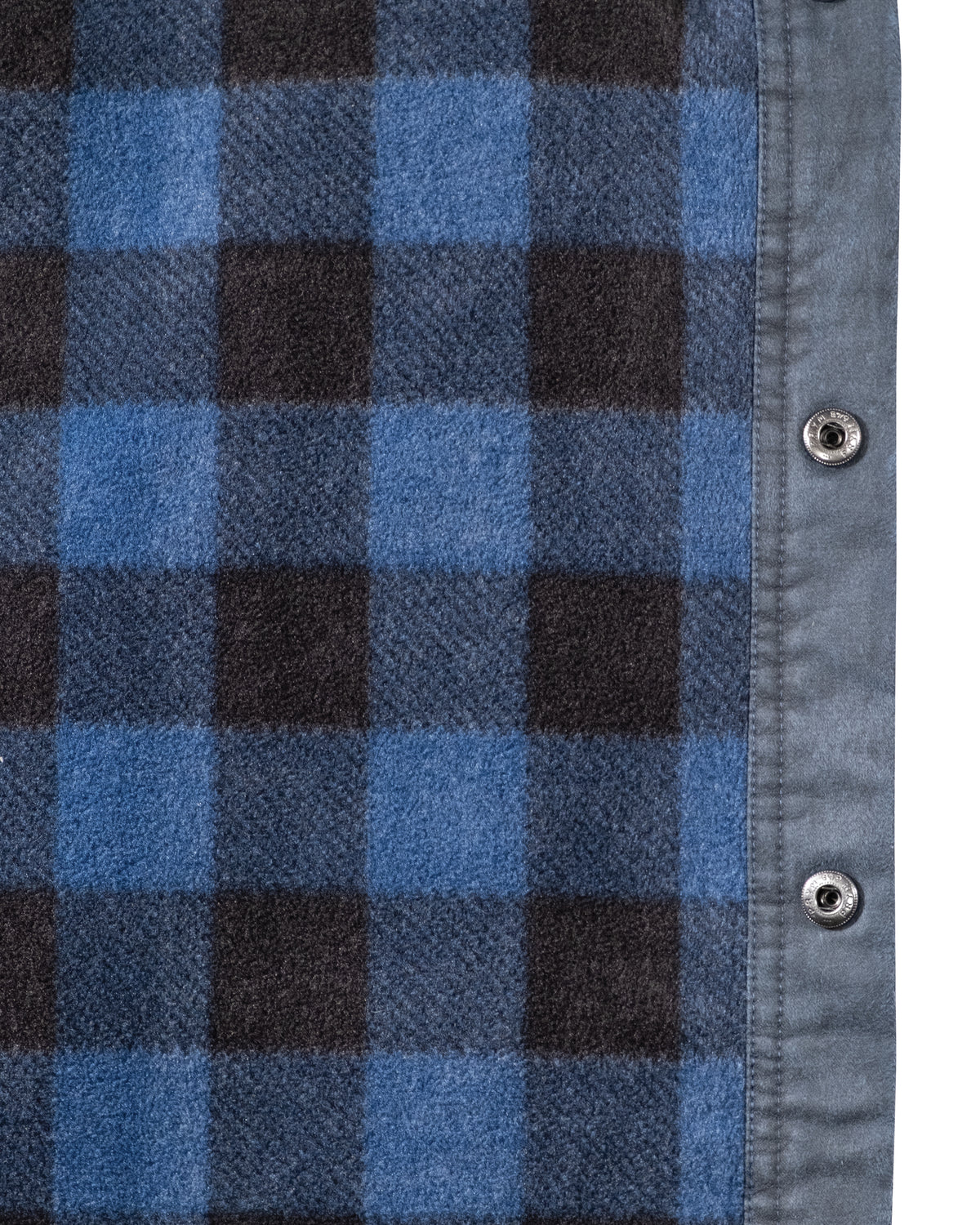 The left side displays a blue and black checkered plaid fabric, while the right reveals part of the Outback Loxton Jacket in gray with two snap buttons, featuring a soft, warm texture similar to fleece lining.