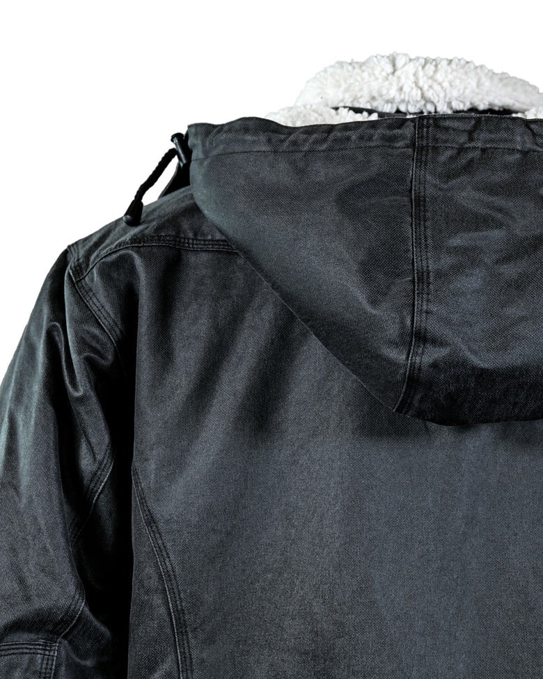 A close-up view of the back of the Outback Nolan Jacket, showcasing its hard-wearing dark gray material. The jacket features visible stitching and a white, fuzzy lining that is partly visible at the top of the hood.