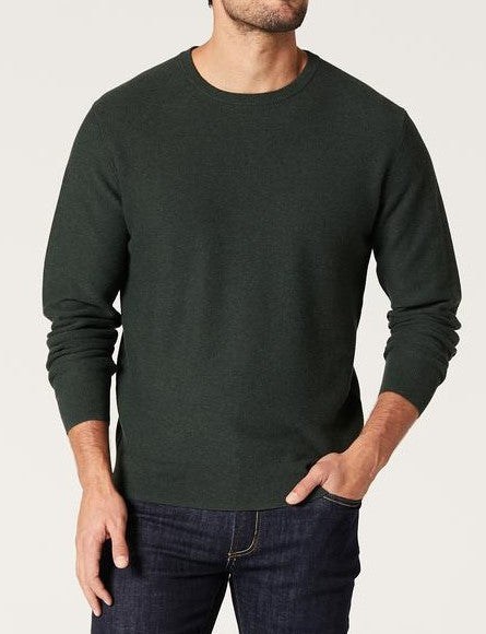 A man wears the Blazer Mason Cotton Textured Crew Neck jumper in dark green with dark blue jeans, standing against a light background. One hand is in his pocket and his face is partially out of frame.