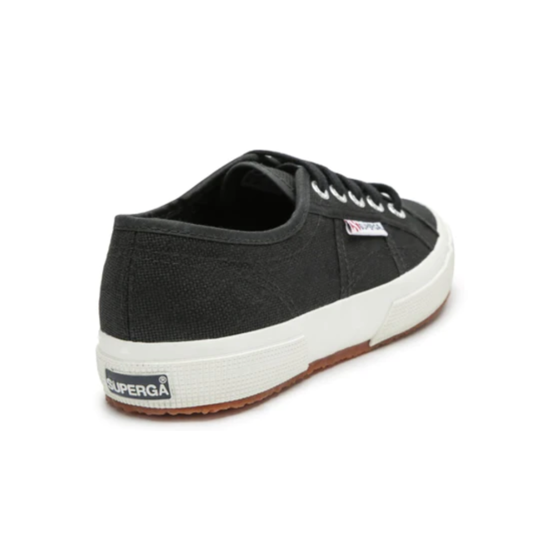 The Superga Cotu Classic Sneaker is black with white laces and a thick sole, featuring the iconic "Superga" logo tag on the heel. Its premium canvas upper has stitching details, and it sports a brown gum sole, embodying Superga's craftsmanship.