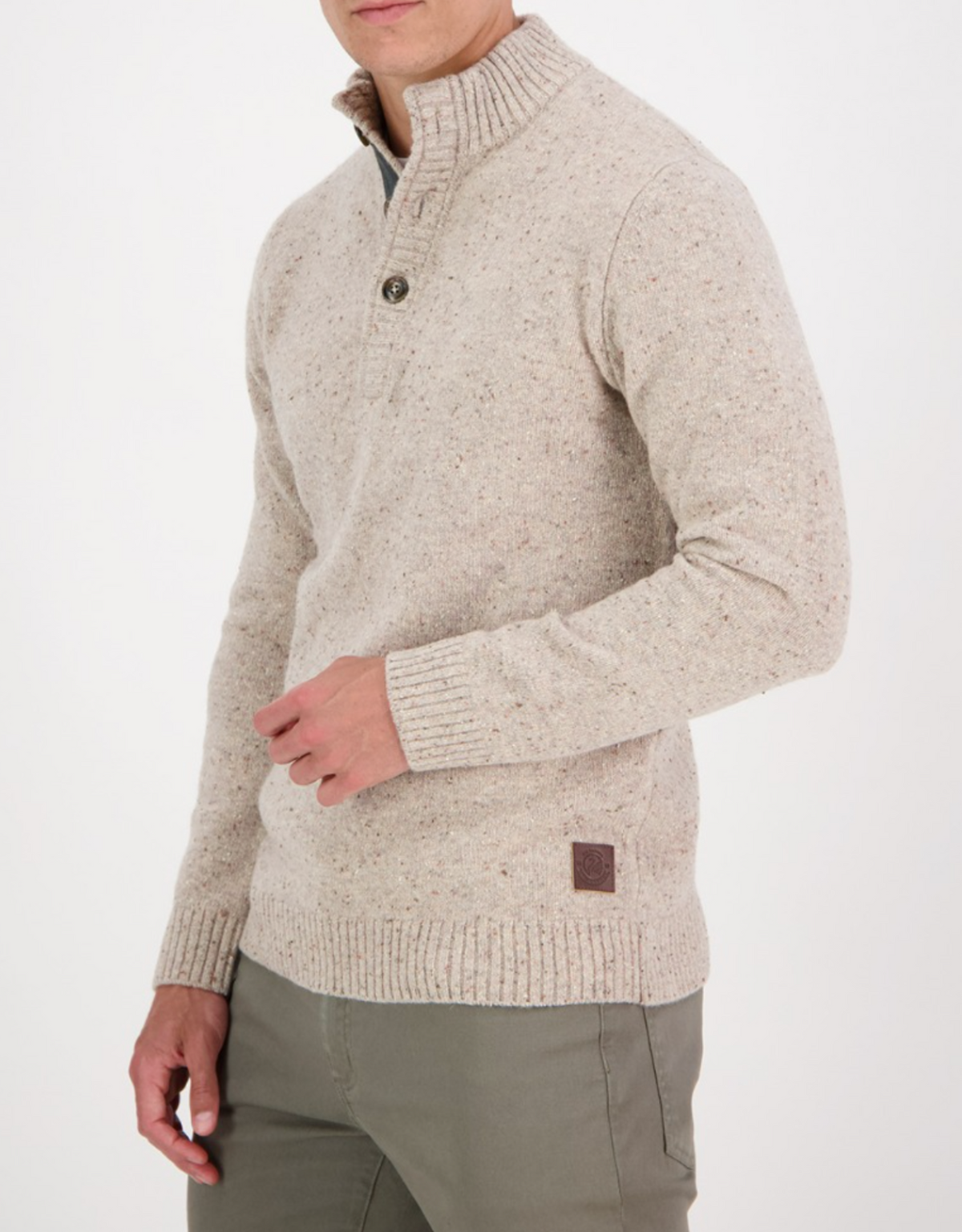 A person wearing the Swanndri Clifton Half Placket Knit in light beige speckled lambswool with a buttoned collar and olive-green pants stands against a plain white background, their head partially out of frame.