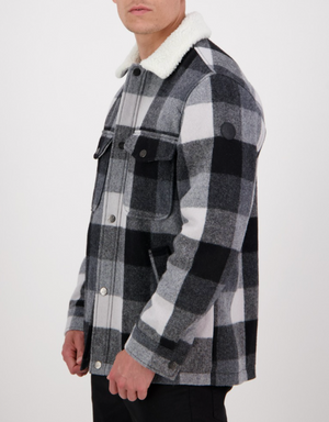 A person stands against a plain background wearing a black and white checkered Swanndri Kaituna Sherpa Lined Jacket, featuring a stylish sherpa lining and white fleece collar, with the jacket neatly buttoned up seen from the side.