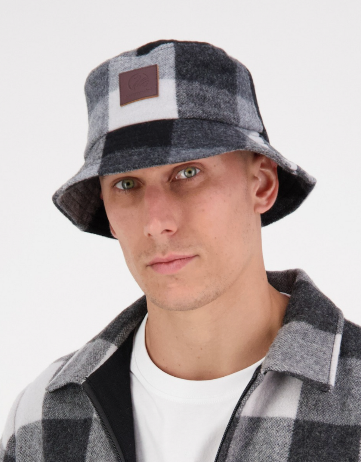 Wearing a Swanndri Kaimai Wool Bucket Hat and a matching checkered jacket over a white shirt, the person gazes directly at the camera against a plain background.