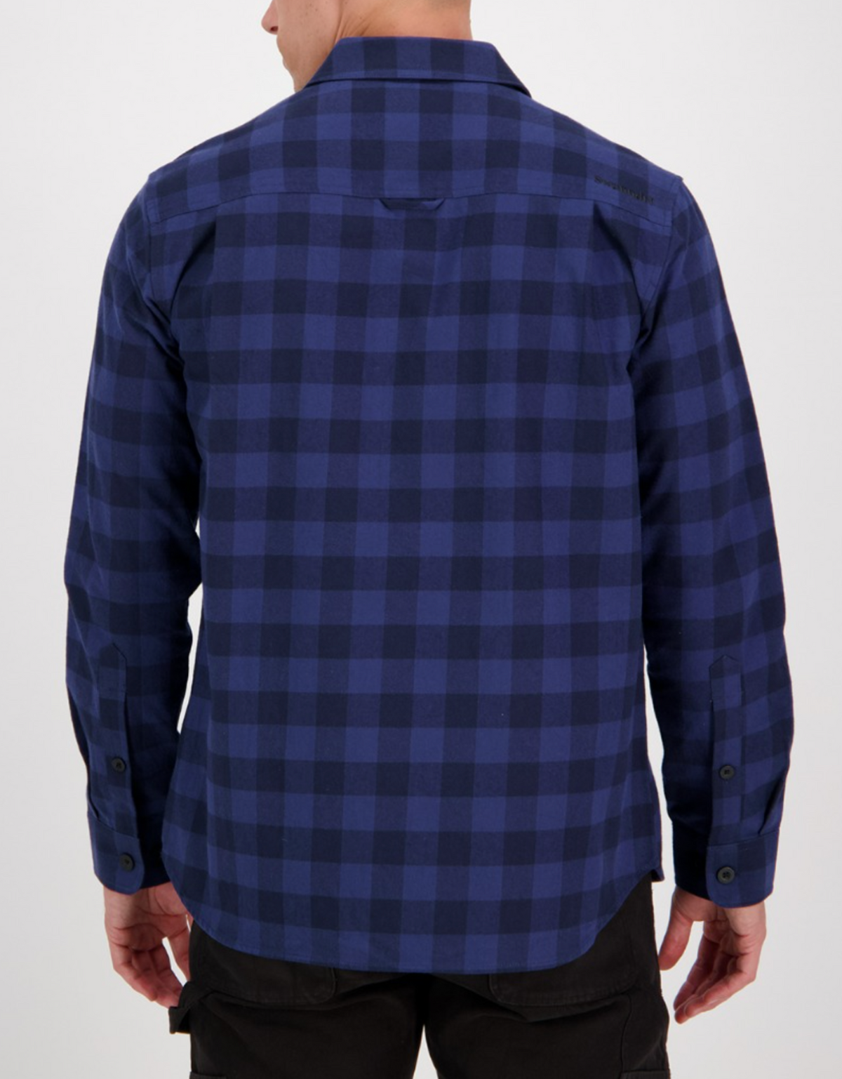 A person, seen from behind, wears the Swanndri Taranaki Tailor Shirt—a stylish long-sleeved blue and black checkered 100% cotton shirt with buttoned cuffs—untucked over dark pants, against a plain light background.