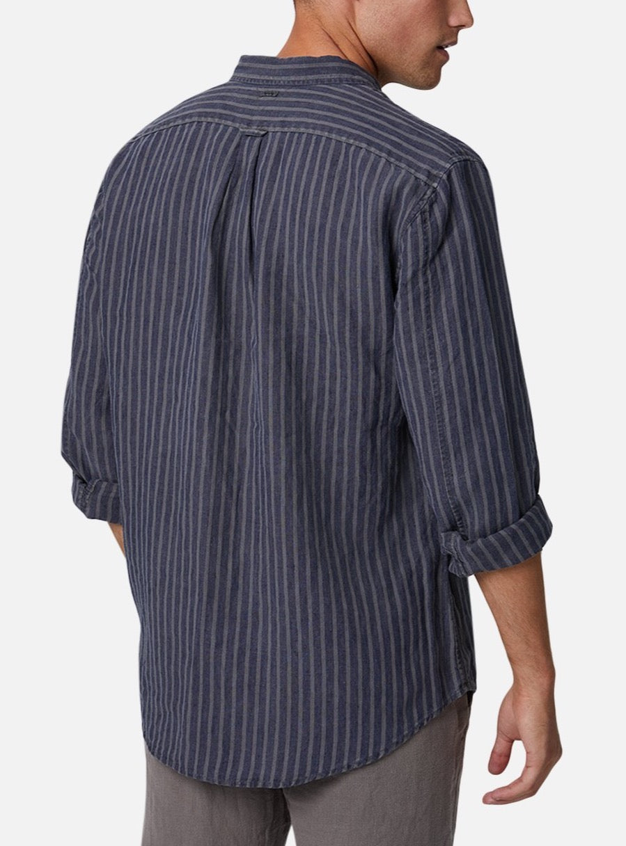 A person is standing with their back to the camera, wearing the Industrie The Chartres L/S Shirt, a long-sleeved, dark blue shirt with vertical stripes. The sleeves are rolled up and the shirt is untucked, displaying its relaxed fit. Made from 100% linen, this casual shirt is paired with grey pants against a plain white background.