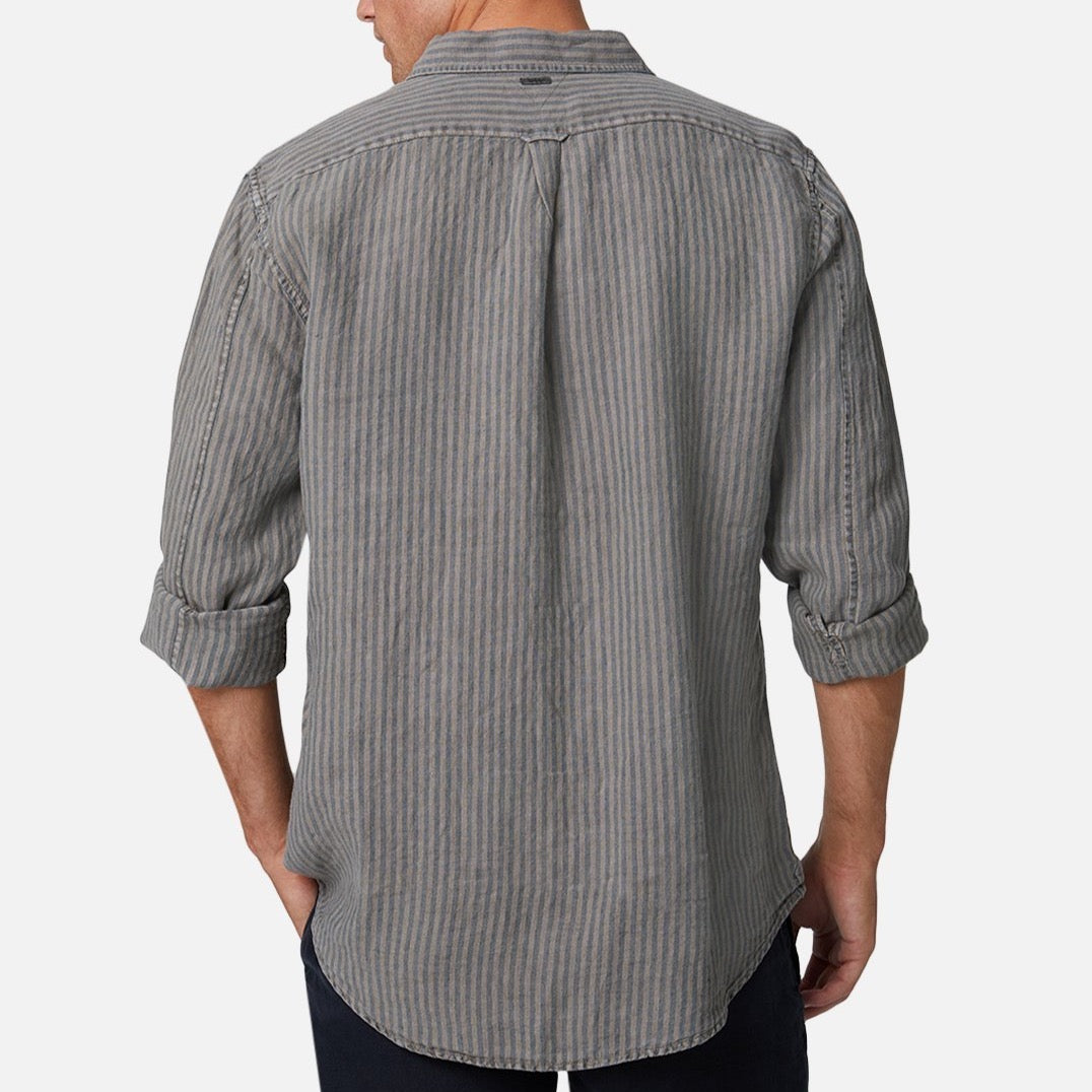 A man stands facing away, wearing the Industrie The Cilento L/S Shirt—a relaxed fit gray and white vertically striped linen shirt with rolled-up sleeves—paired with dark pants, against a plain light background.