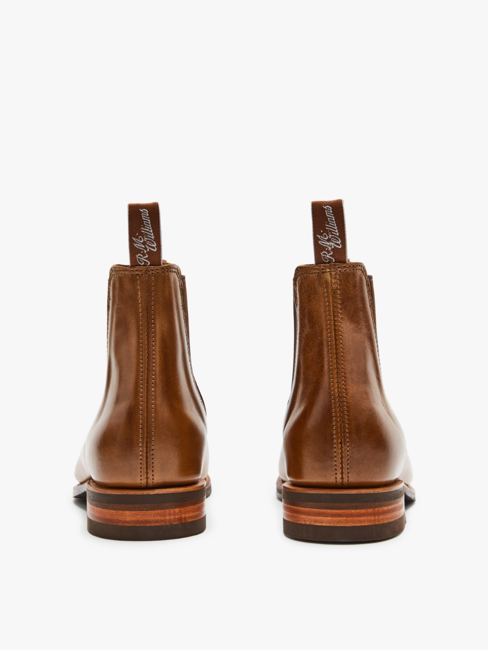 The RM Williams Comfort Craftsman Boot is handmade in Adelaide with brown pull-up leather, pull tabs with white text, and stacked wooden heels. Shown from the back against a plain white background, these Chelsea boots are masterfully crafted.