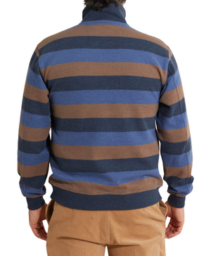 A person wearing the Breakaway Jep French Rib Half Zip, featuring dark blue, brown, and light blue horizontal stripes, faces away from the camera with hands at their sides, elegantly paired with light brown pants.