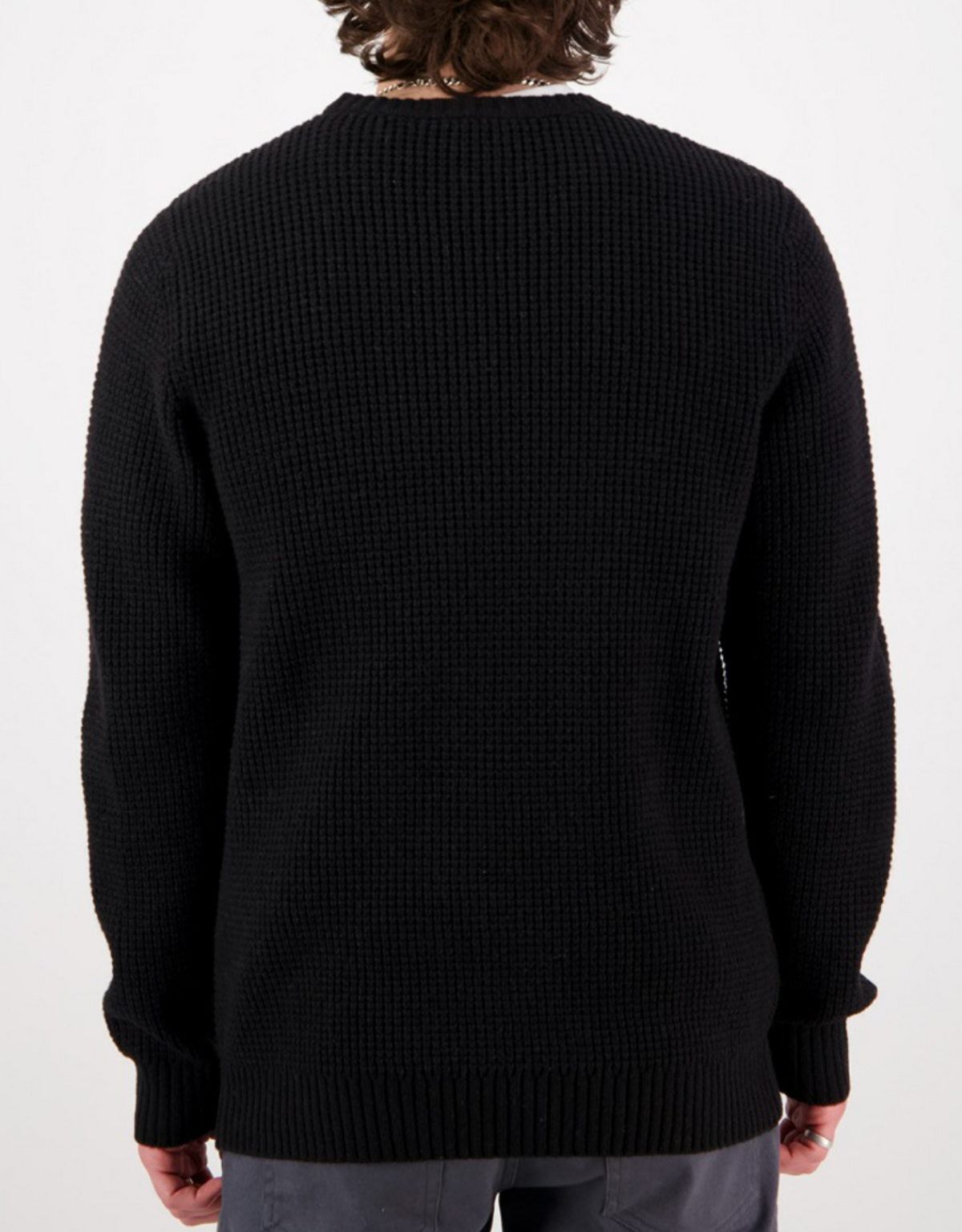 A person with curly brown hair is shown from behind, wearing the Swanndri Fistral Waffle Knit in black and gray pants against a plain white background.
