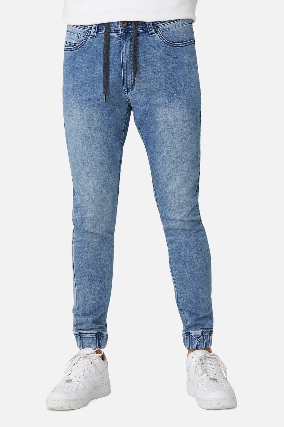 Model wearing the Industrie The Drifter Denim Pant in light blue with a black drawstring, perfectly balancing style and comfort, paired with white sneakers on a white background.