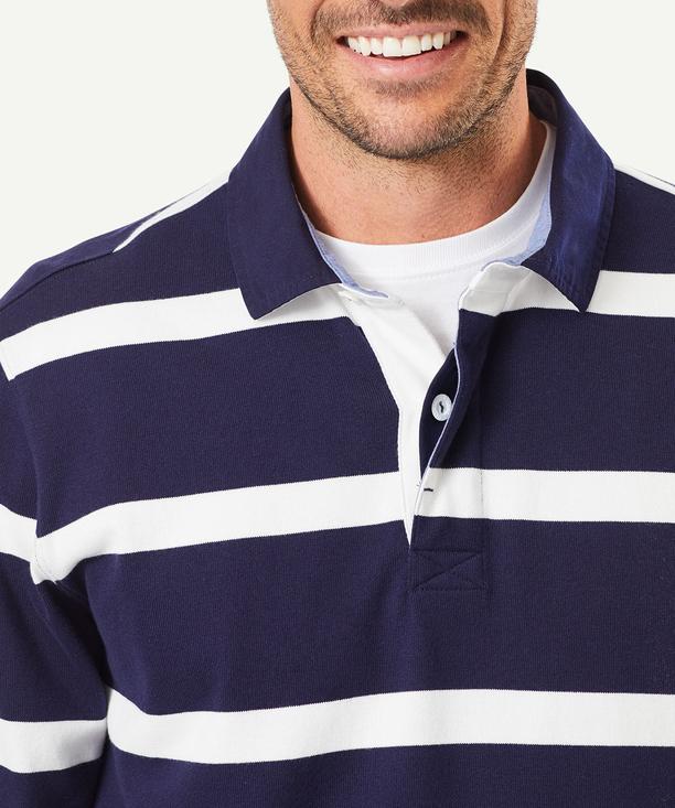 A person wearing a Gazman Classic Stripe Rugby jumper smiles at the camera. The stylish and comfortable shirt features a navy and white striped design with a white collar and three buttons. The image captures the head and upper torso of the person against a plain background.