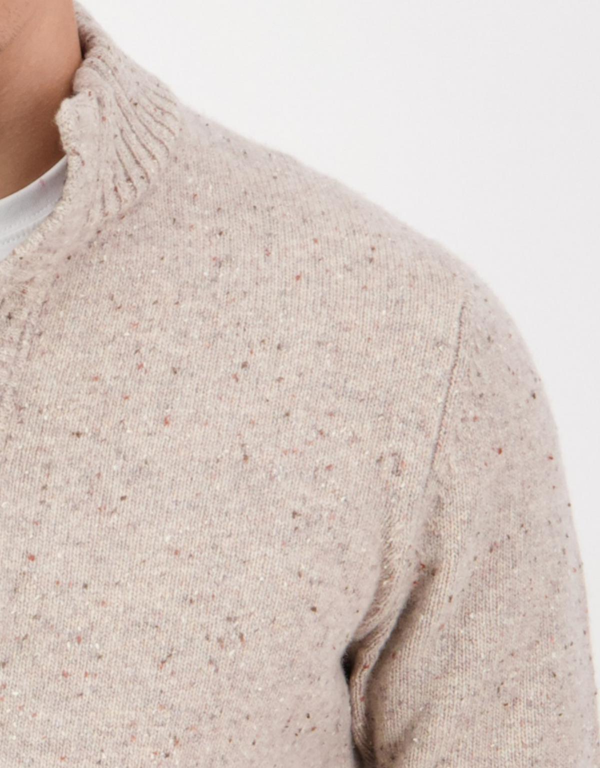 Close-up of a person wearing the Swanndri Clifton Half Placket Knit, a stylish light beige, speckled jumper with a ribbed collar. Only the neck, shoulder, and chest are visible against a plain white background.