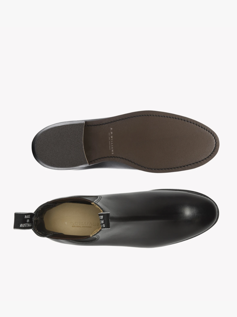 A pair of RM Williams Adelaide Rubber Sole Boots in black leather is displayed. The top boot shows a side view, highlighting the sleek design and pull-tab bearing the "Made in Austria" text. The bottom boot is flipped upside down, showcasing the brown sole and stitching details—reminiscent of Classic Adelaide Boots crafted from Yearling leather.