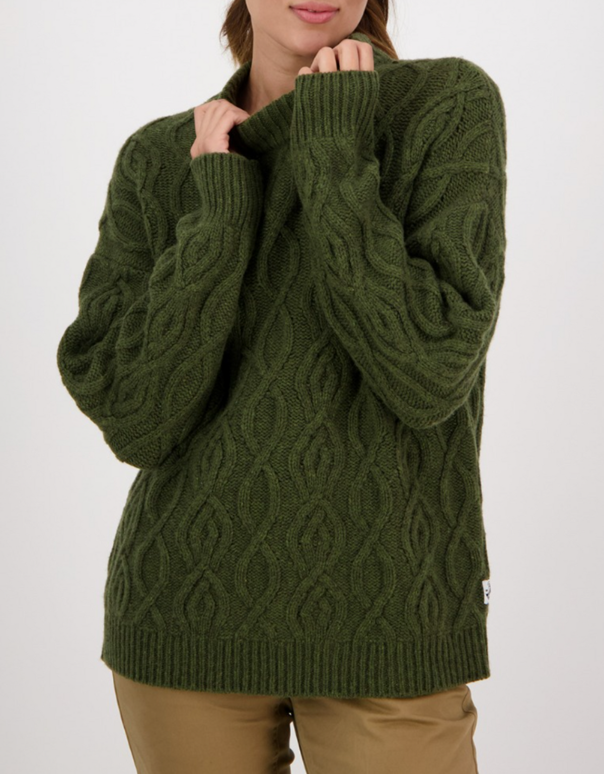 A person wearing the Swanndri Pendeen Cable Neck Crew, an olive green chunky knit sweater with long sleeves and ribbed cuffs, paired with light brown pants, stands against a plain white background.