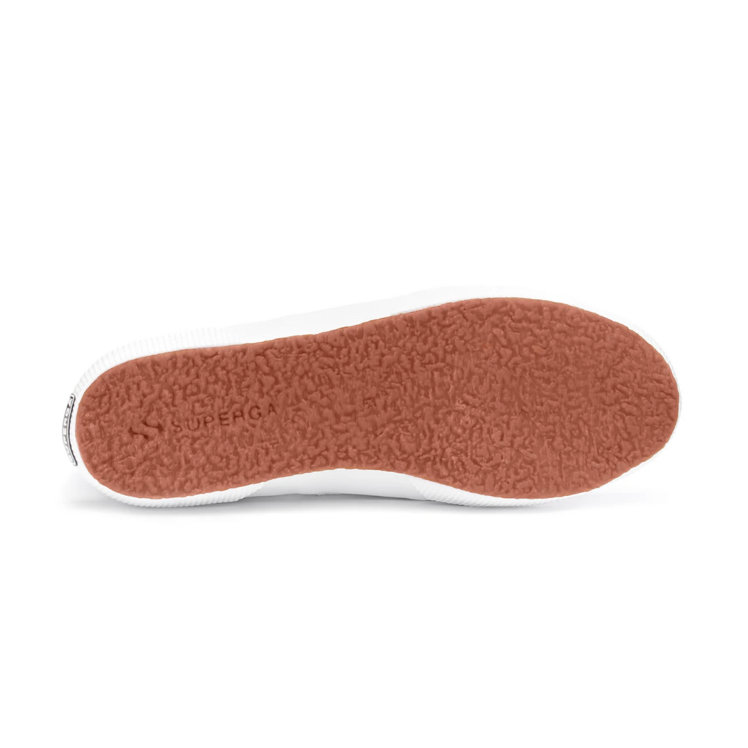 The image shows the Superga Cotu Classic Sneaker's sole, featuring a reddish-brown textured rubber surface with "Superga" embossed. The white edge contrasts, and a canvas upper completes this timeless design.