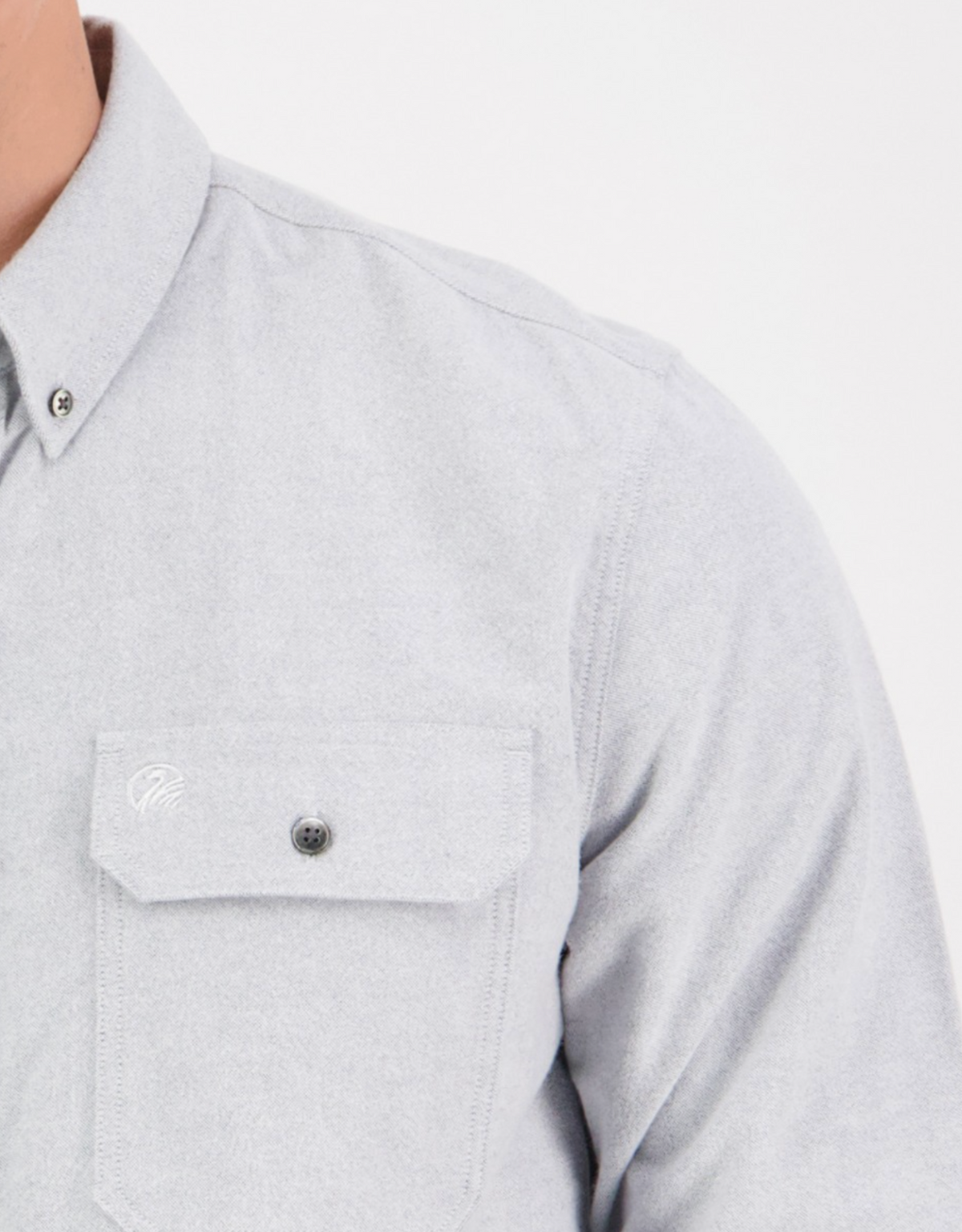 A person wears the Swanndri Marwood Shirt, a stylish light gray button-up with a visible breast pocket. Made from 100% cotton, it features a classic fit with collar and subtle stitching. The photo focuses on the upper body.