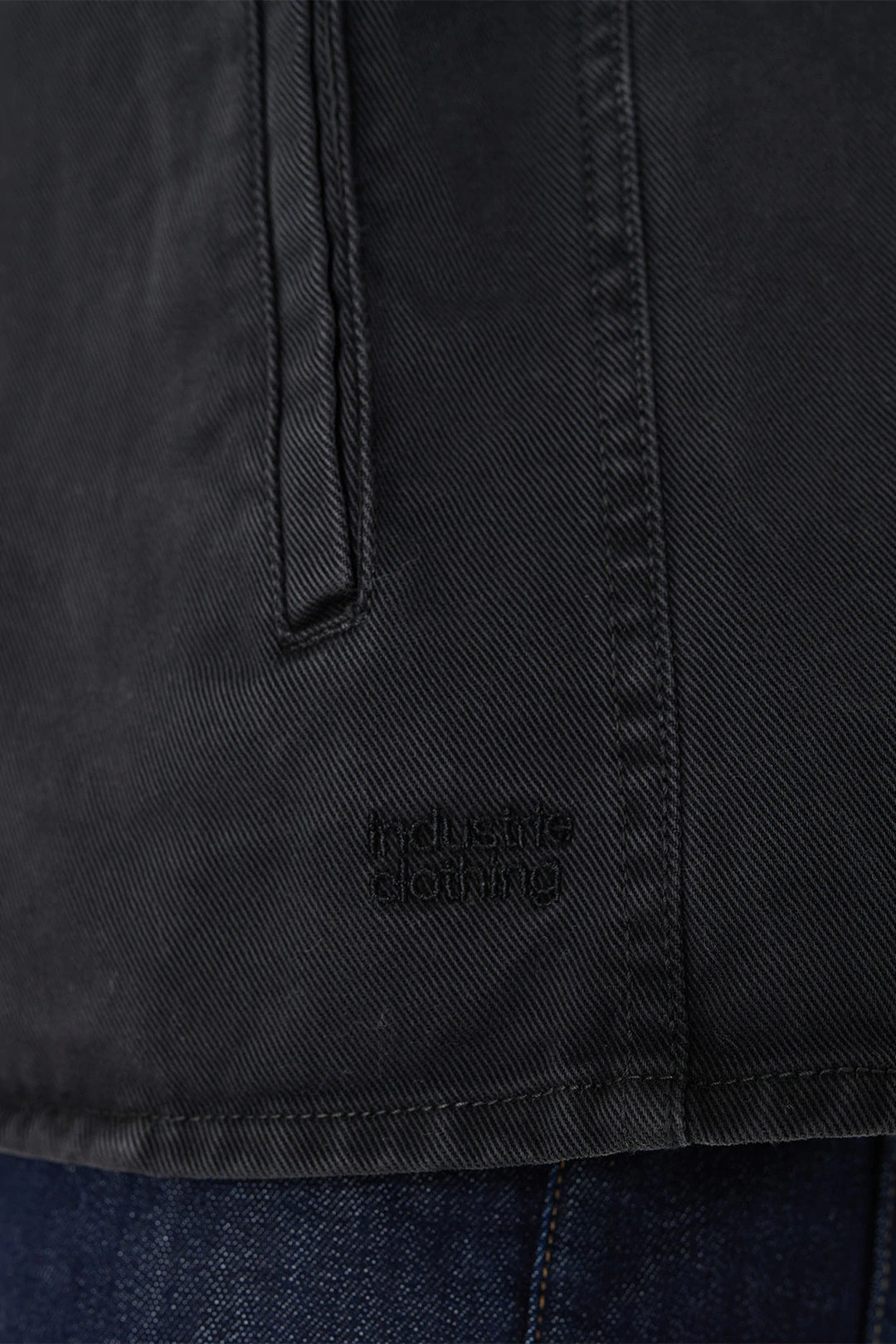 Close-up of a black cotton Industrie The Woodbury Shirt with a vertical pocket and stitching detail. "Industrié Clothing" is subtly displayed on the fabric. Comfortable and stylish, it pairs effortlessly with dark blue denim jeans for a chic look.