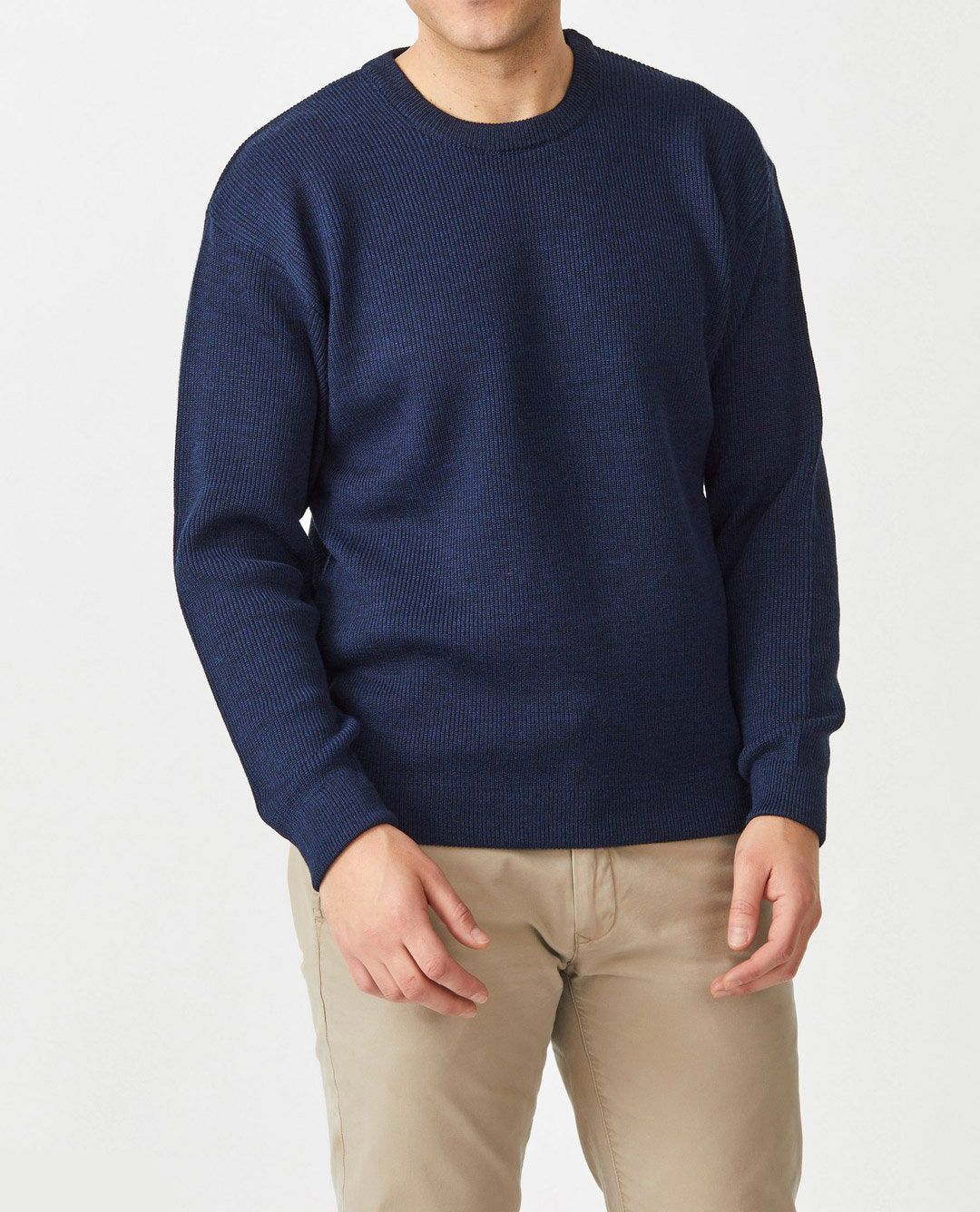 A person in an Aklanda Fishermans Rib Crew Pullover made of Australian Made merino wool, dark blue in color, paired with beige pants, stands against a white background. The face is not shown.