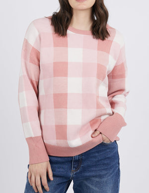 A person wears a Foxwood Julissa Crew, a pink and white checkered crew neck sweater with ribbed hem and cuffs, paired with blue jeans against a plain background. Their face is not visible.