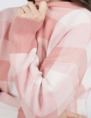 Wearing a cozy Foxwood Julissa Crew, a pink and white checkered sweater with ribbed cuffs, someone partially covers their face with their hand.