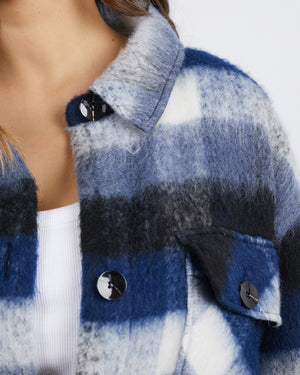 Close-up of a person wearing the Foxwood Nellie Jacket, featuring large black buttons and a stylish plaid flannel over a white top. The soft, textured fabric resembles a wool coat. The image focuses on the shoulder and upper torso area.