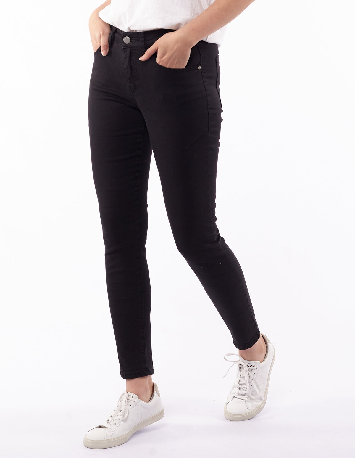A person wearing a white shirt and Foxwood City Jeans in black stands in a relaxed pose. They are sporting white sneakers with white laces against a plain white background.
