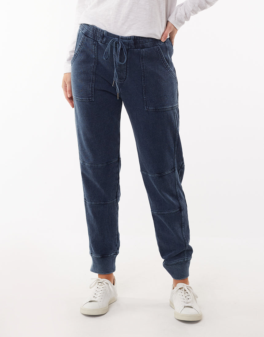 A person wearing a white long-sleeve shirt and a pair of Foxwood Annie Pants with an elastic waist and visible seam details. The comfortable pants, reminiscent of a denim wash, are paired with white sneakers. The image is cropped from the shoulders down against a plain white background.