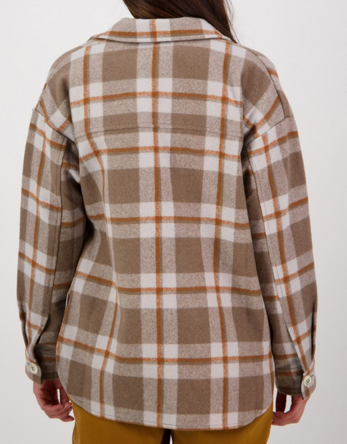 A person with long hair is facing away from the camera, wearing a brown, white, and orange Swanndri Anchorage Wool Shirt Jacket over yellow pants. The jacket, reminiscent of a classic Swanndri with its buttoned cuffs, stands out against the plain white background.