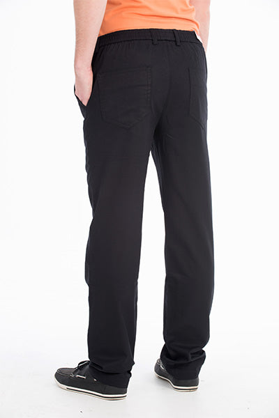 A person stands facing away, wearing the Bob Spears Pull On Pant, which features an elastic waist and back pockets. The comfortable pants appear to be made of a soft fabric and are paired with an orange shirt. The person’s hands are in their pockets, and they are wearing black sneakers with white soles. The background is plain white.