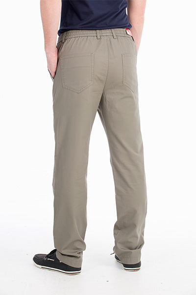 A person stands facing away, wearing Bob Spears Pull On Pants in light brown featuring an elastic waistband and patch pockets, paired with a dark-colored shirt tucked in. They also sport black sneakers with white soles against a plain white background.