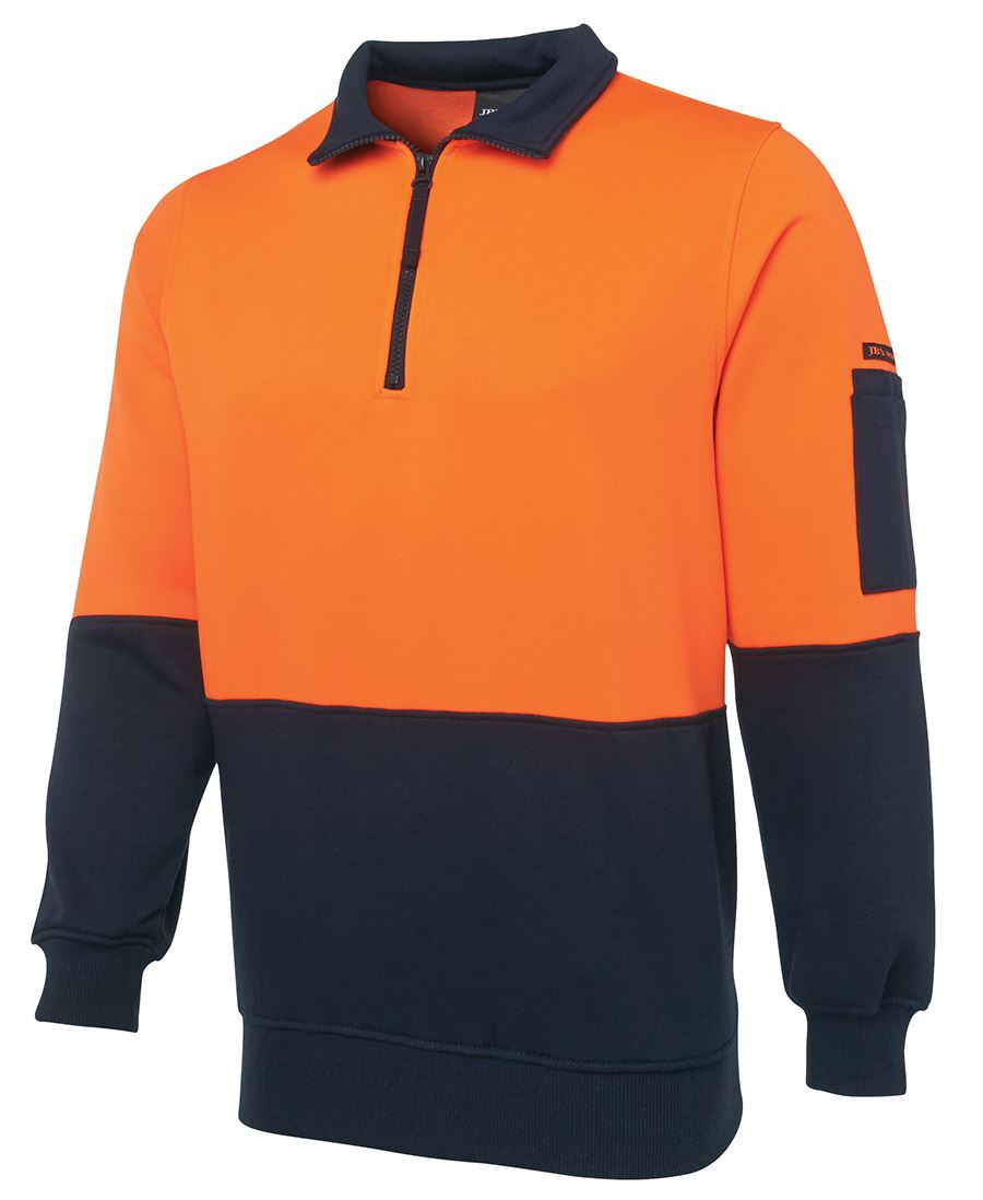 The JBs Hi Vis 1/2 Zip Fleecy is a high-visibility pullover sweatshirt featuring a half-zip collar. The top portion of this durable polyester cotton garment is bright orange, while the bottom, including the sleeves and cuffs, is dark navy. Additionally, it has a small flap pocket on the upper left sleeve designed for workwear essentials.