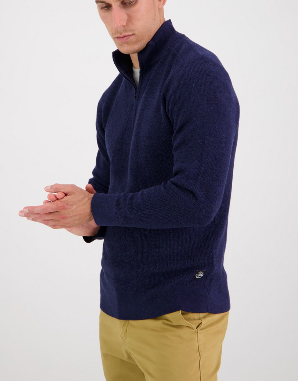 A man wears the Swanndri Magnet Bay v2 Merino Jumper in navy blue with khaki pants, standing against a plain white background and looking down with his hands together.