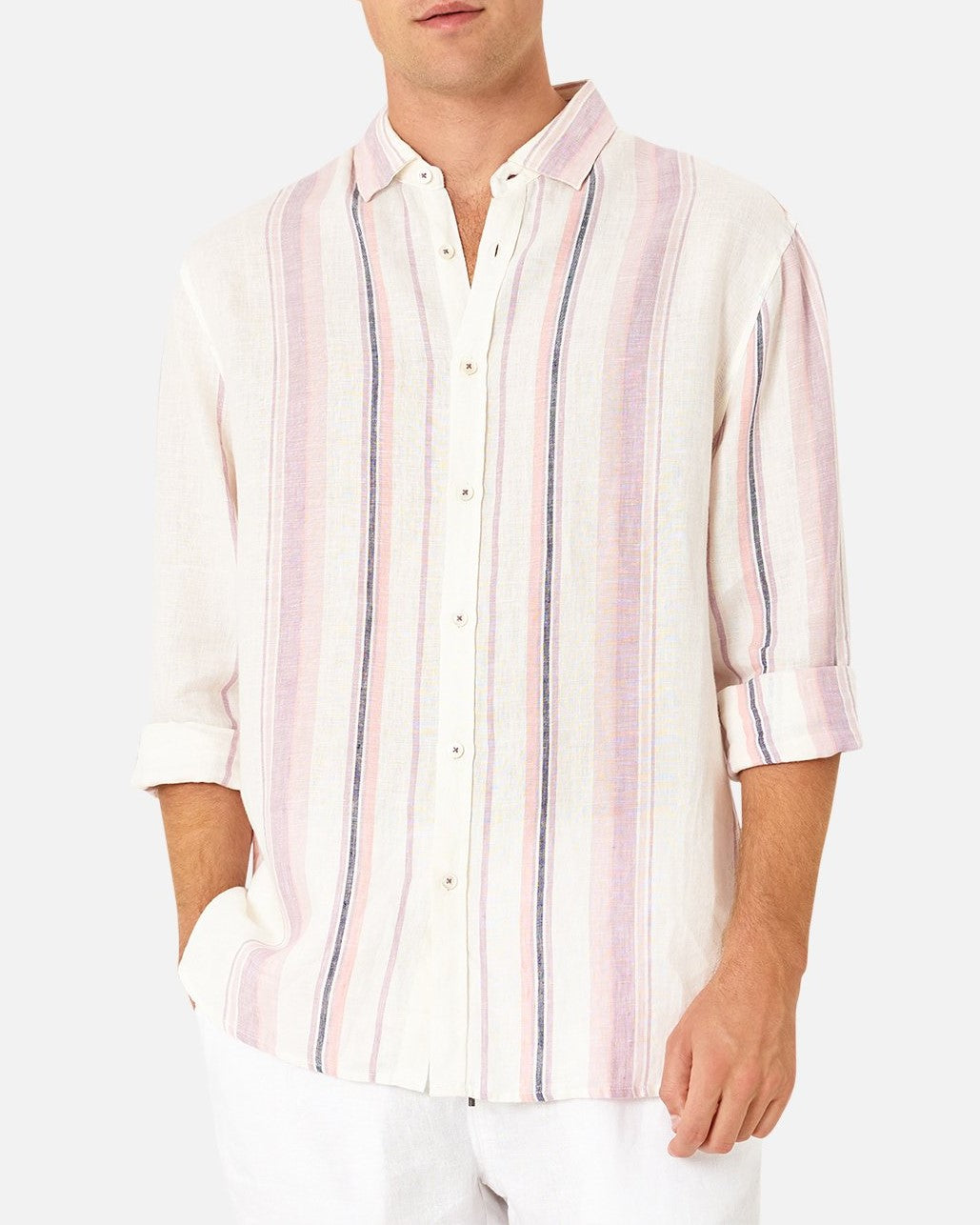 A person is modeling the Industrie The Beechwood Linen Long Sleeve Shirt with sleeves rolled up to the elbows. This classic fit, comfortable shirt is made from 100% linen and features vertical stripes in shades of pink, white, and light blue. The person has their hands in their pockets and is wearing white pants against a plain white background.