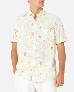 A person wearing the Industrie The Esperanza Shirt, a casual classic fit short-sleeve button-up in light pastel floral print with yellow and pink flowers, features a small left-side pocket. Made from 100% Rayon, set against a plain white background.