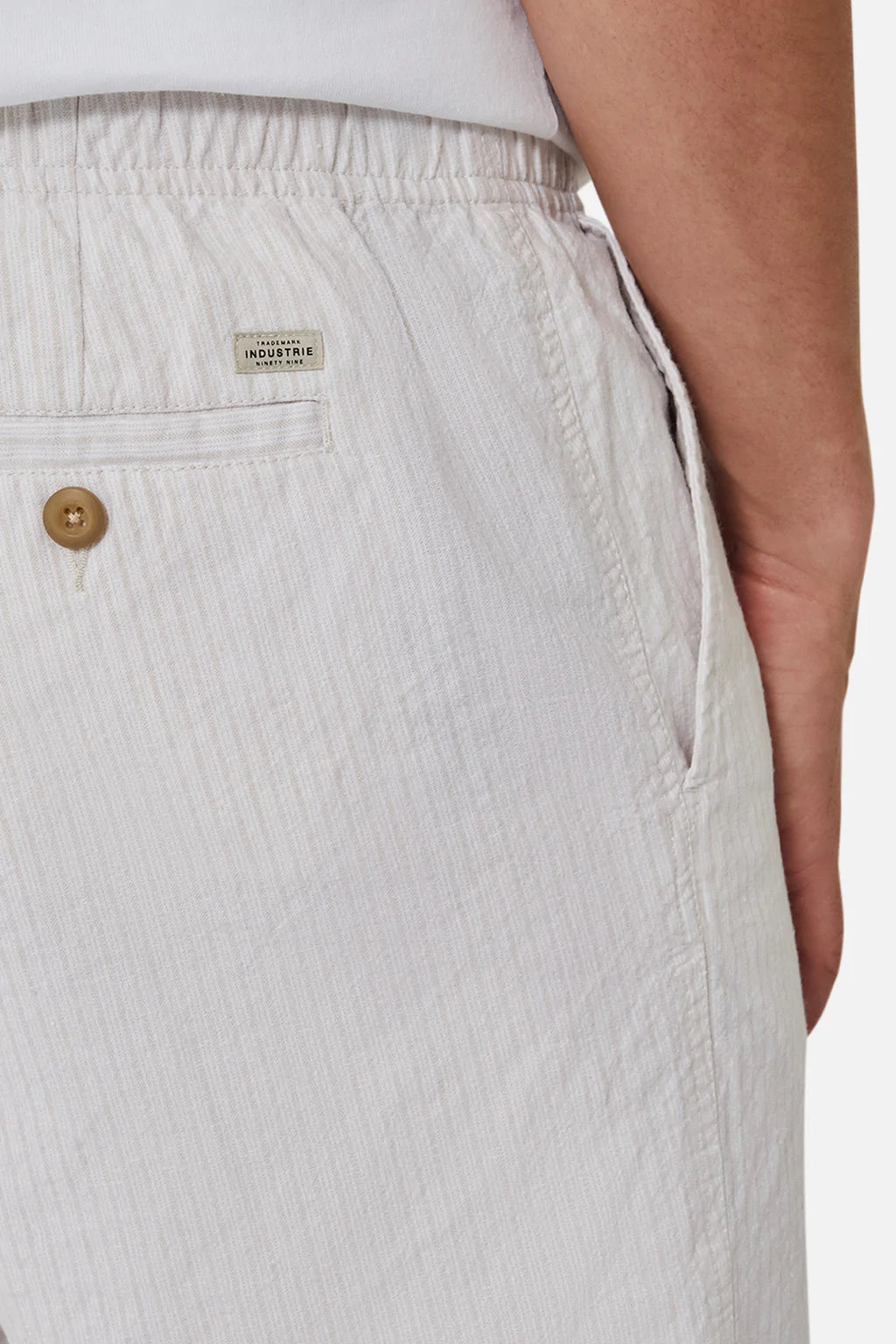 Close-up of someone wearing Industrie The Elio Short in linen cotton with vertical stripes, featuring an elasticised waistband, side and buttoned back pocket. A small tag near the waistband reads "Industry.