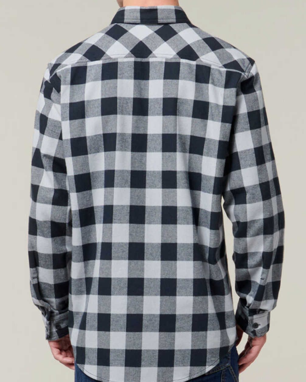 A person wearing a Hard Yakka Check Flannelette Shirt made of black and white checkered 100% Cotton Twill is standing with their back facing the camera. The long-sleeve shirt features a pattern of large squares. The individual is also wearing blue jeans.
